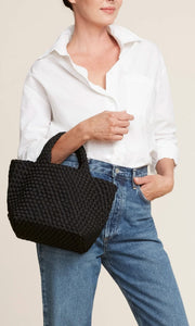 Woman standing with Naghedi handwoven neoprene St. Barths Small Tote bag in Onyx, available at Amara Home.